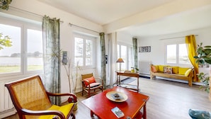 A spacious living room with large windows, a wooden sofa, a red coffee table, and a wicker chair. - Gorgeous apartment in Locmariaquer with WiFi (Locmariaquer)
