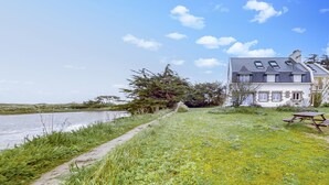 A house with a grassy lawn, a picnic table, and a body of water in the background. - Gorgeous apartment in Locmariaquer with WiFi (Locmariaquer)