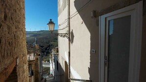 A narrow alleyway with a stone wall on one side and a building with a white door and window on the other. A street lamp is visible in the distance. - B&B Black & White (Pietramontecorvino)