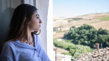Une personne se tient près d’une fenêtre, d’où l’on peut admirer un paysage rural.