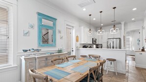 Una cocina amplia con una mesa de comedor de madera, armarios blancos e iluminación colgante.