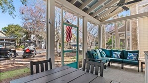 Un patio techado con una mesa y sillas, un sofá verde con cojines azules, y una bandera estadounidense.