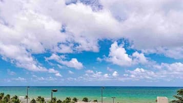 Une vue sur la côte, avec un ciel dégagé, une plage et un espace de stationnement équipé de lampadaires.