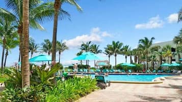 Un espace piscine aménagé dans un complexe hôtelier, avec des palmiers, des chaises longues et des parasols.
