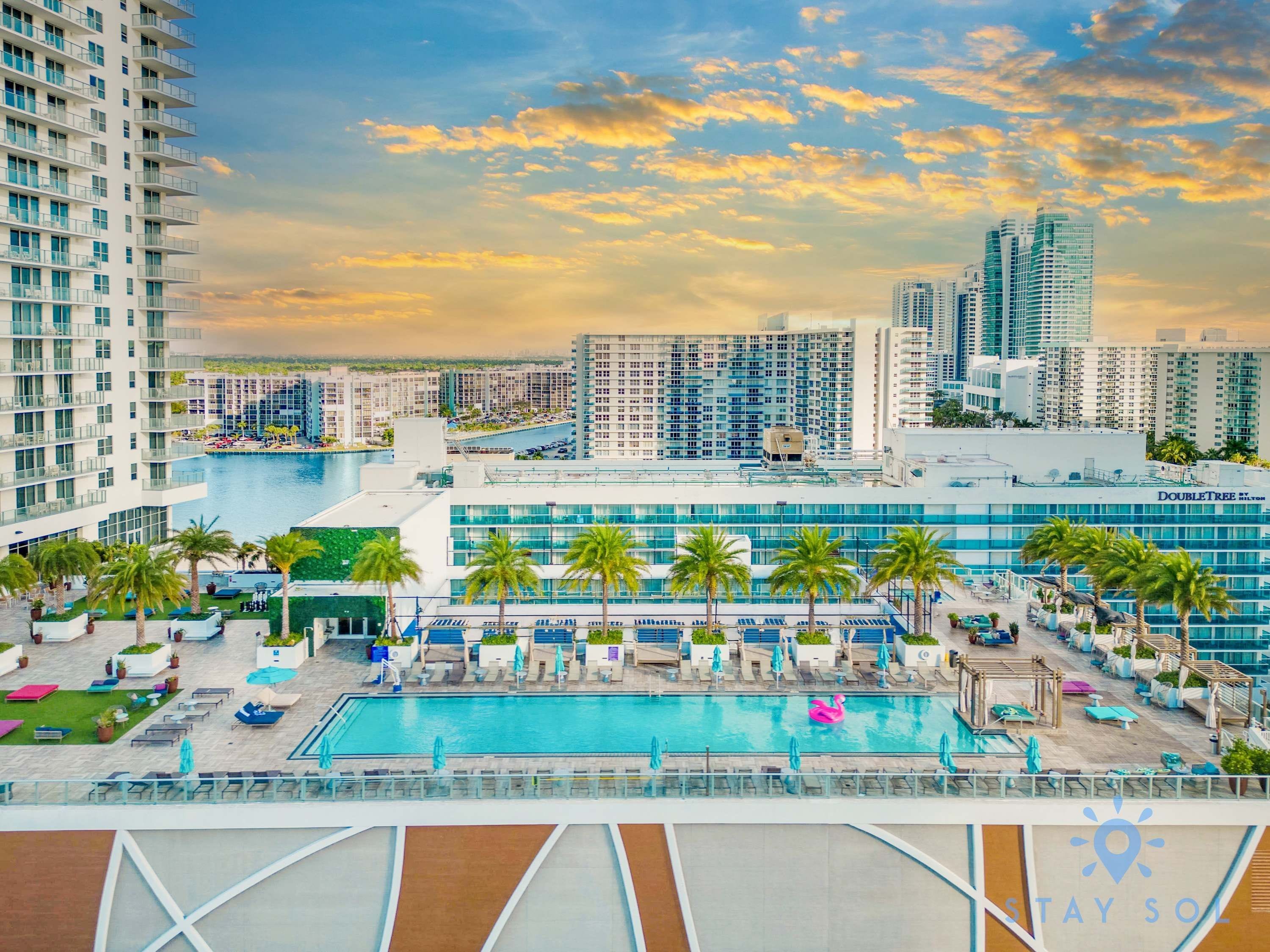A hotel with a pool, palm trees, and a cityscape in the background.