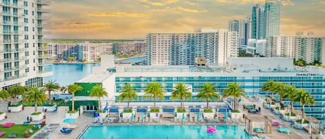 A hotel with a pool, palm trees, and a cityscape in the background.