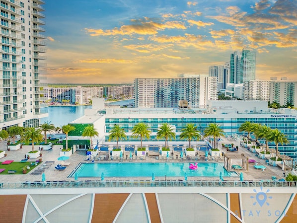 A hotel with a pool, palm trees, and a cityscape in the background.