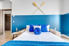 A bedroom with a bed, pillows, a blue wall, and two wooden paddles mounted on the wall.