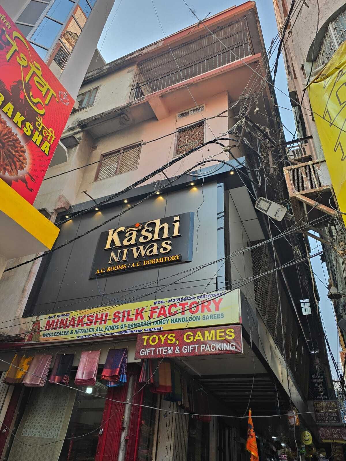 Un edificio con varios letreros, incluyendo uno que indica 'Kashi Niwas A.C. Dormitory' y otro que anuncia 'Minakshi Silk Factory'.