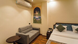 Una habitació d'hotel amb un llit, un sofà gris, una taula rodona petita, un aparell d'aire condicionat i un penjament decoratiu a la paret.