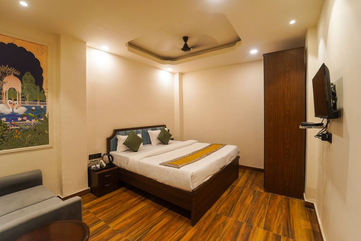 A hotel room with a bed, a nightstand, a television, and a painting on the wall.