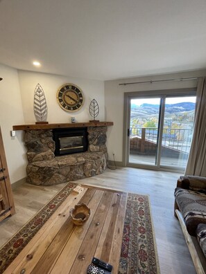 A living room with a stone fireplace, a wooden coffee table, and a sofa. - Rustic Ski-In Condo Under the Mountain (Crested Butte)