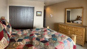 Een slaapkamer met een groot bed, een houten dressoir, een spiegel en een deur.