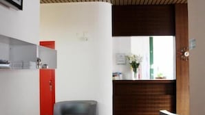 Een moderne receptie met een plafond van houten latten, een rode balie en een grijze bank.