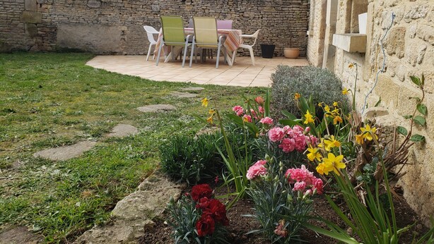 Un muro de piedra, un patio con mesa y sillas, y un jardín con flores.