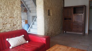 Un sofá de cuero rojo con un cojín blanco, una mesa de centro de madera, una pared de piedra, un aparador de madera y una escalera que conduce a un segundo piso.