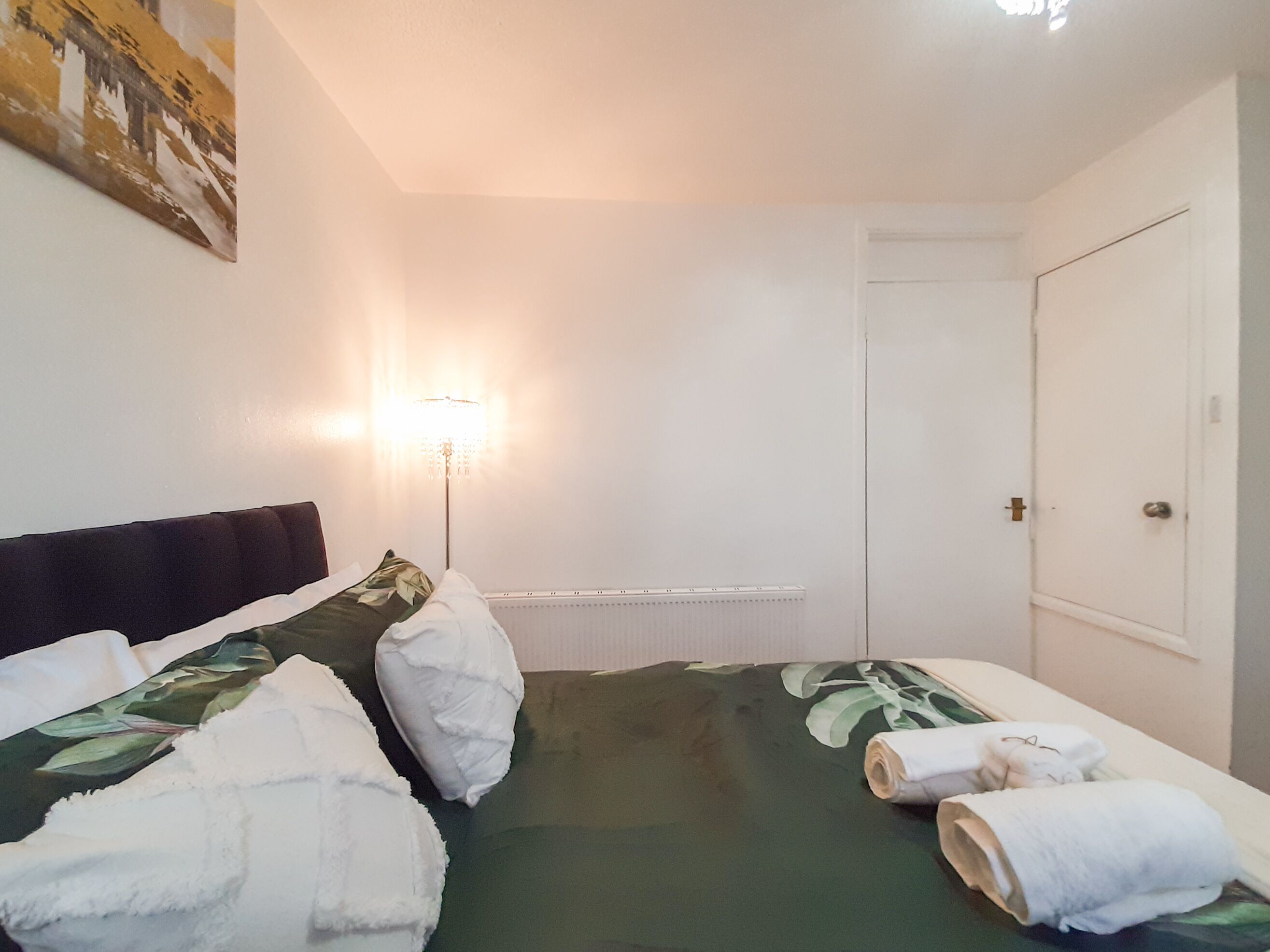 A hotel room with a bed, a nightstand, a lamp, and a door.