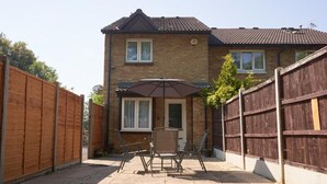 A two-story house with a patio area featuring a table and chairs, a wooden fence, and a satellite dish. - I Luv London Too! 1bed Stunnin Home Sleeps 3! (London)