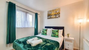 A neatly made bed with green bedding, a bedside table with a lamp, and a window with curtains. - I Luv London Too! 1bed Stunnin Home Sleeps 3! (London)