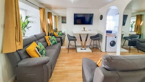 A modern living room with a grey sofa set, a dining table with two chairs, a TV mounted on the wall, and a washing machine in the corner. - I Luv London Too! 1bed Stunnin Home Sleeps 3! (London)