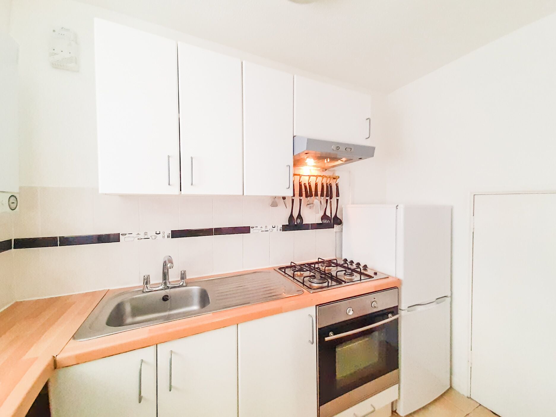 A compact kitchen with white cabinets, a stainless steel sink, a gas stove, and a built-in oven.