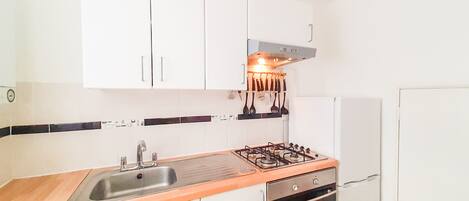 A compact kitchen with white cabinets, a stainless steel sink, a gas stove, and a built-in oven.
