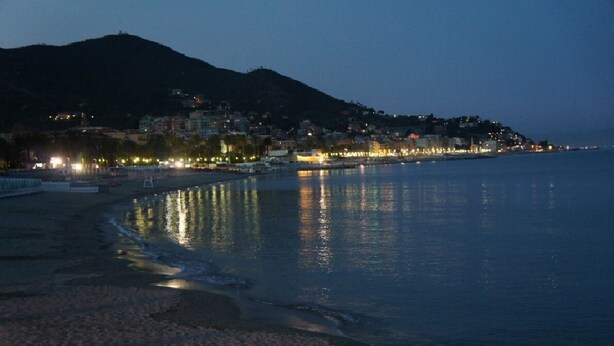 A coastal cityscape at dusk with buildings along the waterfront and a beach in the foreground. - Hotel Lido (Varazze)