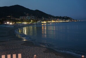A coastal cityscape at dusk with buildings along the waterfront and a beach in the foreground. - Hotel Lido (Varazze)