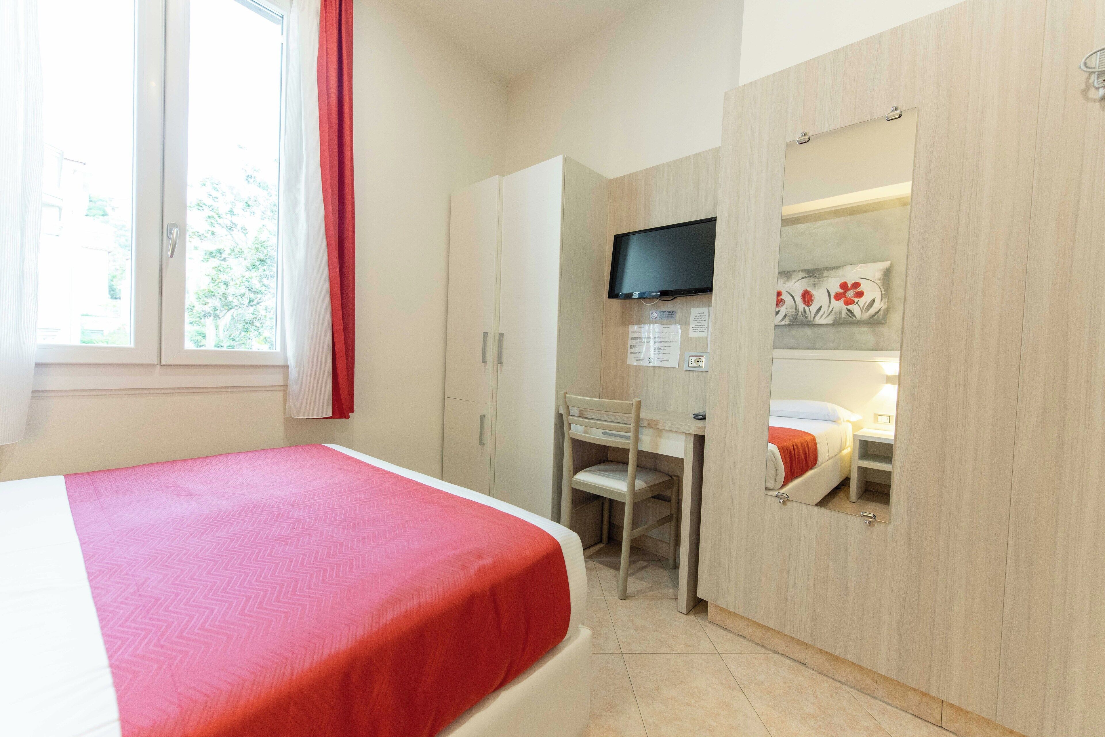 Une chambre à coucher avec un lit, un bureau, une télévision et une armoire.