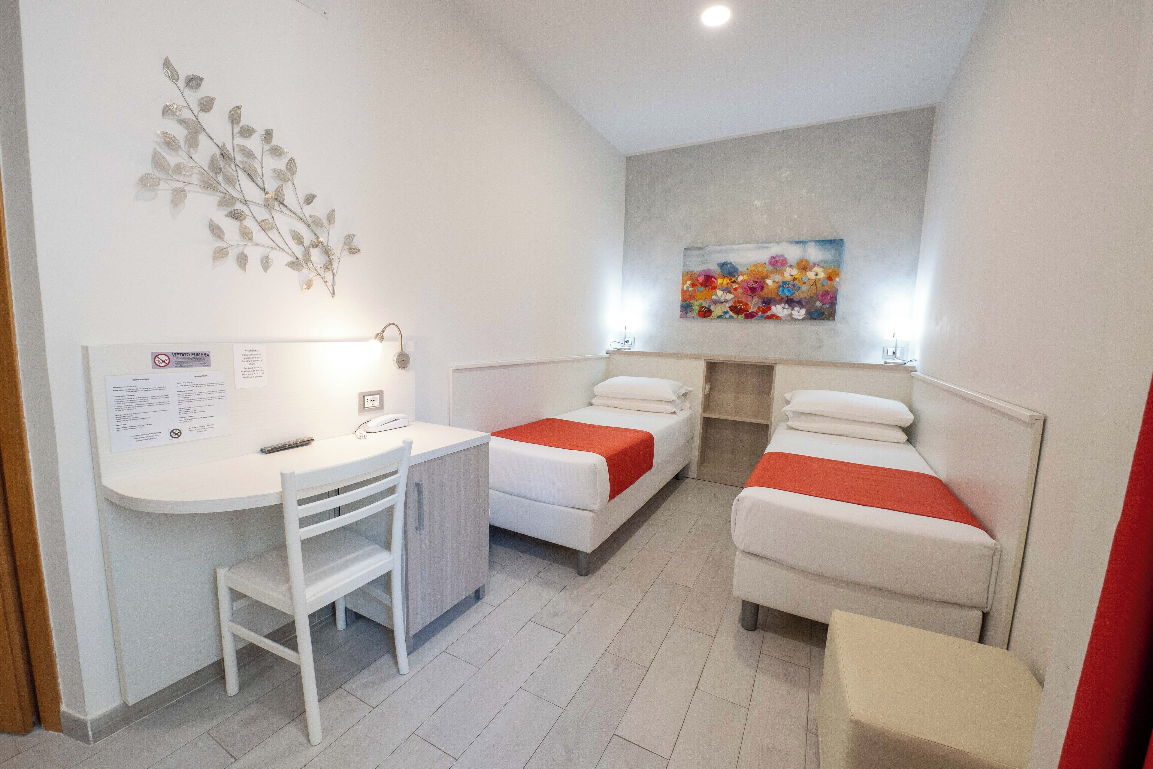 Una habitación pequeña y moderna con escritorio, dos camas y un cuadro en la pared.