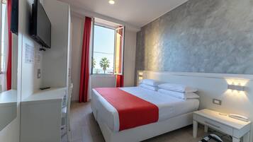 Ein Hotelzimmer mit einem Bett, einem Nachttisch und einem an der Wand befestigten Flachbildfernseher.