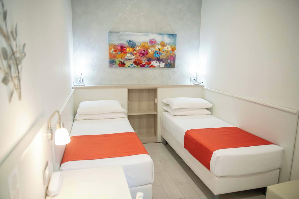 Habitación de hotel con dos camas individuales, un escritorio pequeño y un cuadro en la pared.