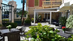 An outdoor patio area with wicker furniture, potted plants, and a covered seating area. - Hotel Lido (Varazze)