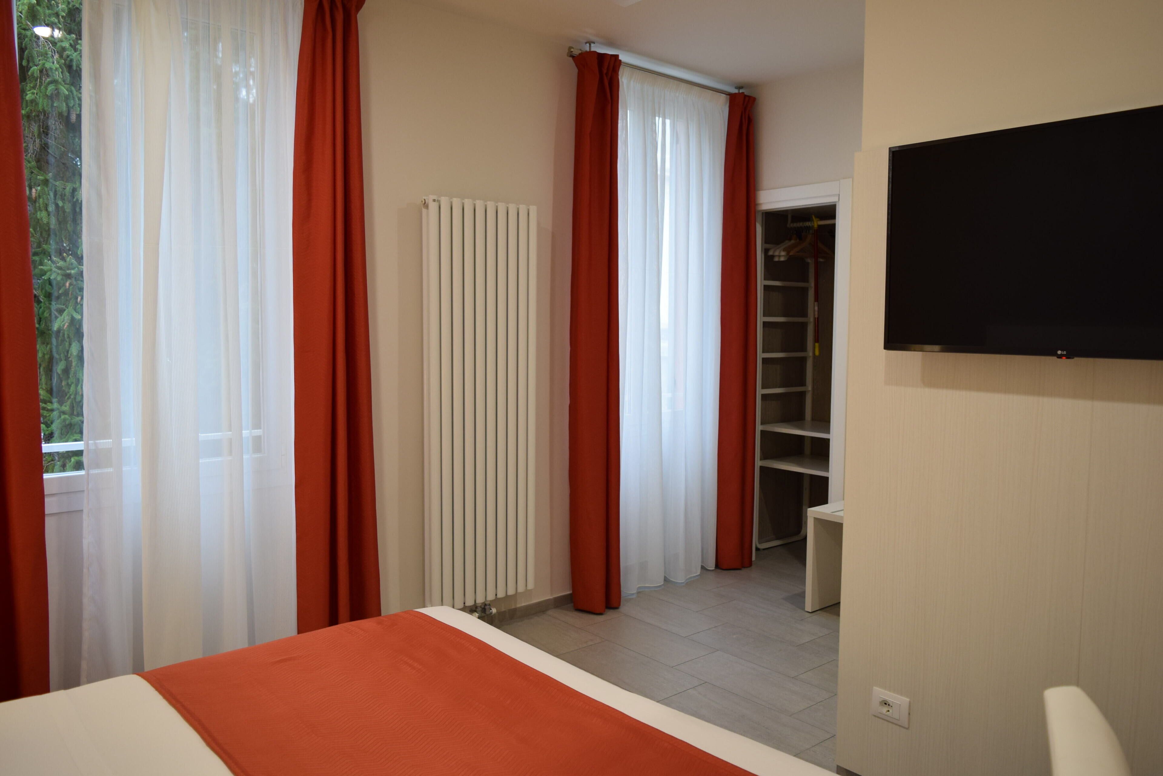 A hotel room with a bed, a radiator, a closet, and a television.