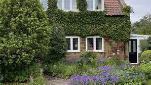 A stone house with ivy-covered walls, a garden with various flowers, and a paved pathway.