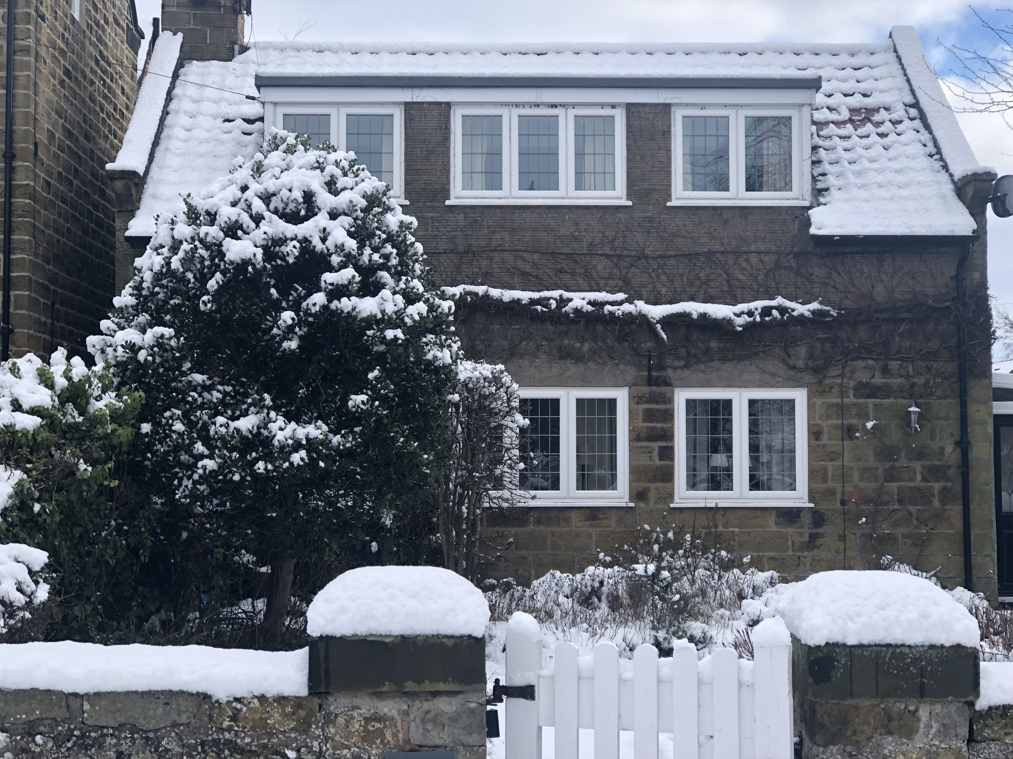 A two-story stone house with a white picket fence and snow-covered surroundings.