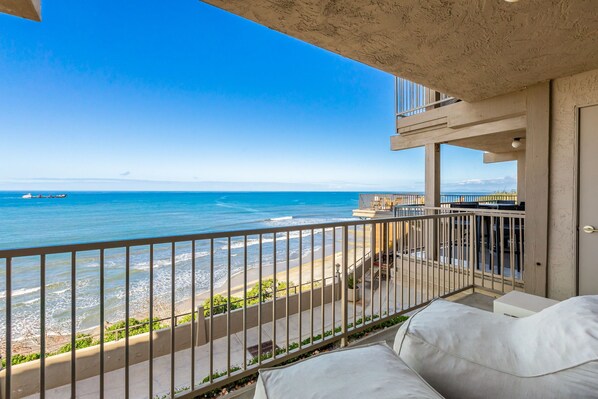 A balcony with a view of the ocean, a white sofa, and a small table. - Del Mar Beach Club Condo with Ocean Views & Pool (Solana Beach)