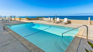 A rooftop pool with clear blue water, surrounded by lounge chairs and potted plants, overlooking a calm sea. - Del Mar Beach Club Condo with Ocean Views & Pool (Solana Beach)