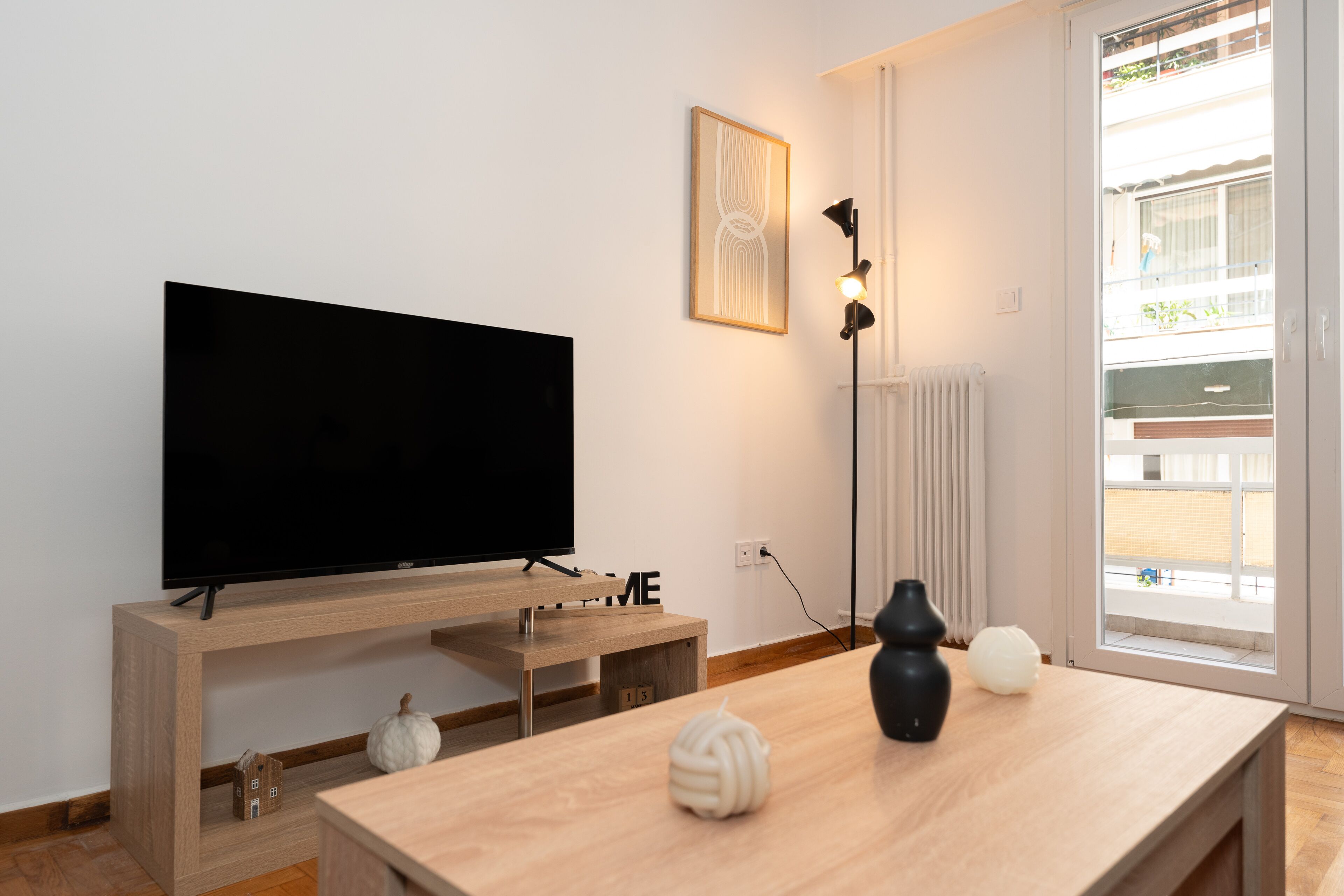 A modern living room with a flat-screen TV on a wooden stand, a small house-shaped decoration, and a couple of spherical objects on a wooden table.