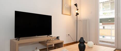 A modern living room with a flat-screen TV on a wooden stand, a small house-shaped decoration, and a couple of spherical objects on a wooden table.