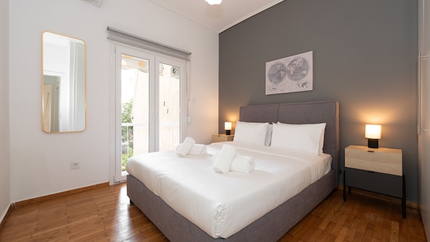 Quarto moderno com uma cama grande, luminárias de cabeceira, um espelho e vista através de uma porta de vidro.