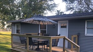 Eine Holzterrasse mit Tisch und Stühlen, ein überdachter Patio-Bereich und eine kleine Treppe, die zu einem Haus führt.