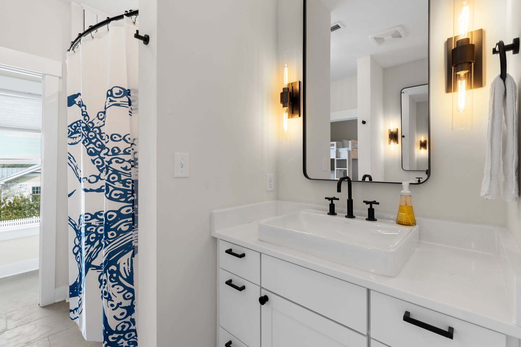 A modern bathroom with a white sink, black faucet, and a shower curtain with a blue pattern.