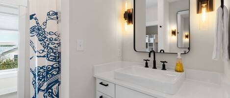 A modern bathroom with a white sink, black faucet, and a shower curtain with a blue pattern.