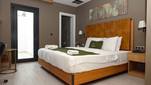 A modern hotel room with a wooden bed, a small bedside table, a chair, a door to a balcony, and a painting on the wall. - Garden Mode Airport Hotel (Arnavutköy)