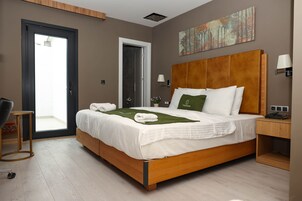 Una habitación de hotel moderna con una cama de madera, una mesita de noche pequeña, una silla, una puerta a un balcón y un cuadro en la pared.