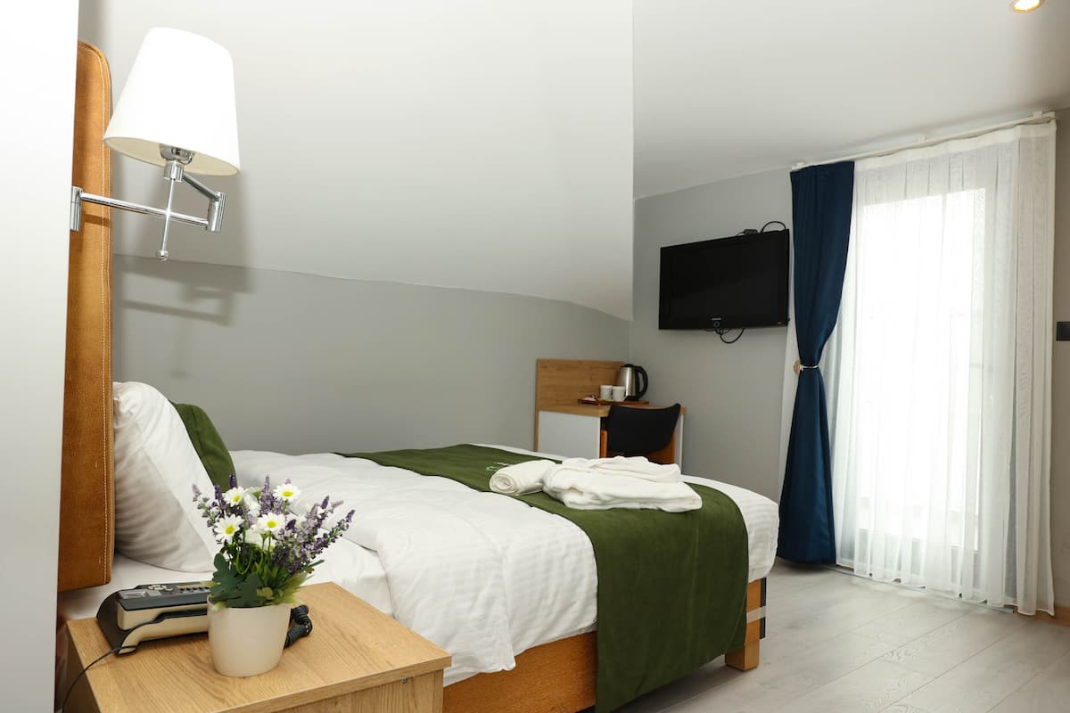 Una cama bien hecha con una manta verde, una mesita de noche con una lámpara, un control remoto y un florero.