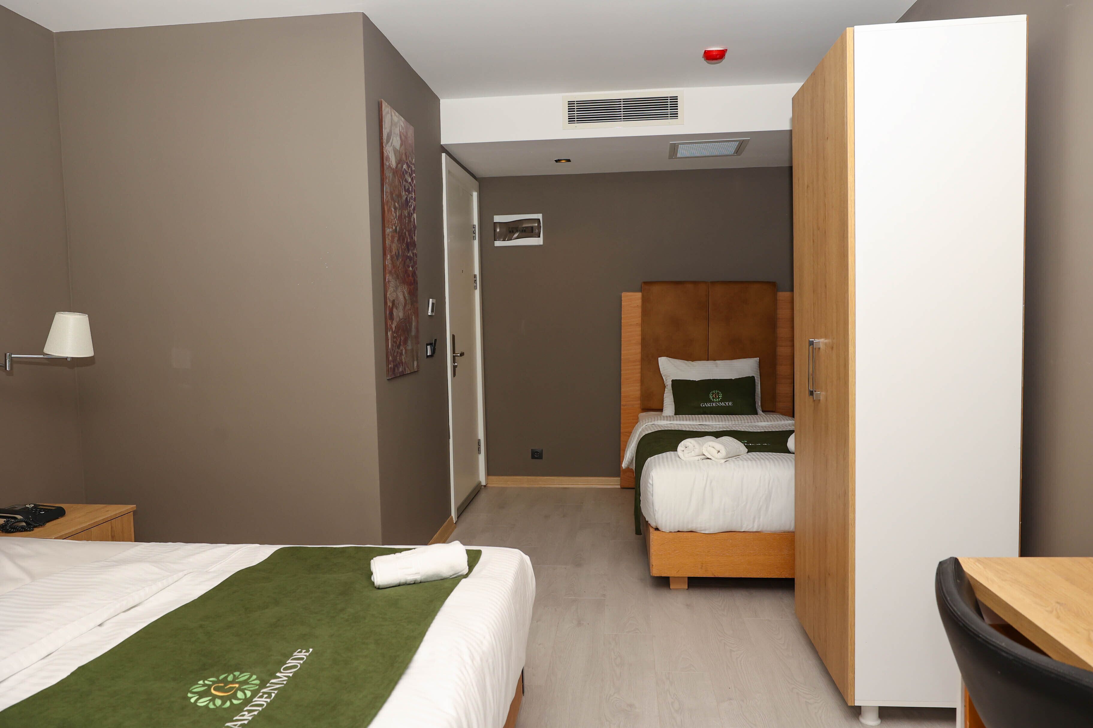 A hotel room with two beds, a wooden wardrobe, a desk, and a chair.
