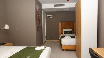 A hotel room with two beds, a wooden wardrobe, a desk, and a chair.