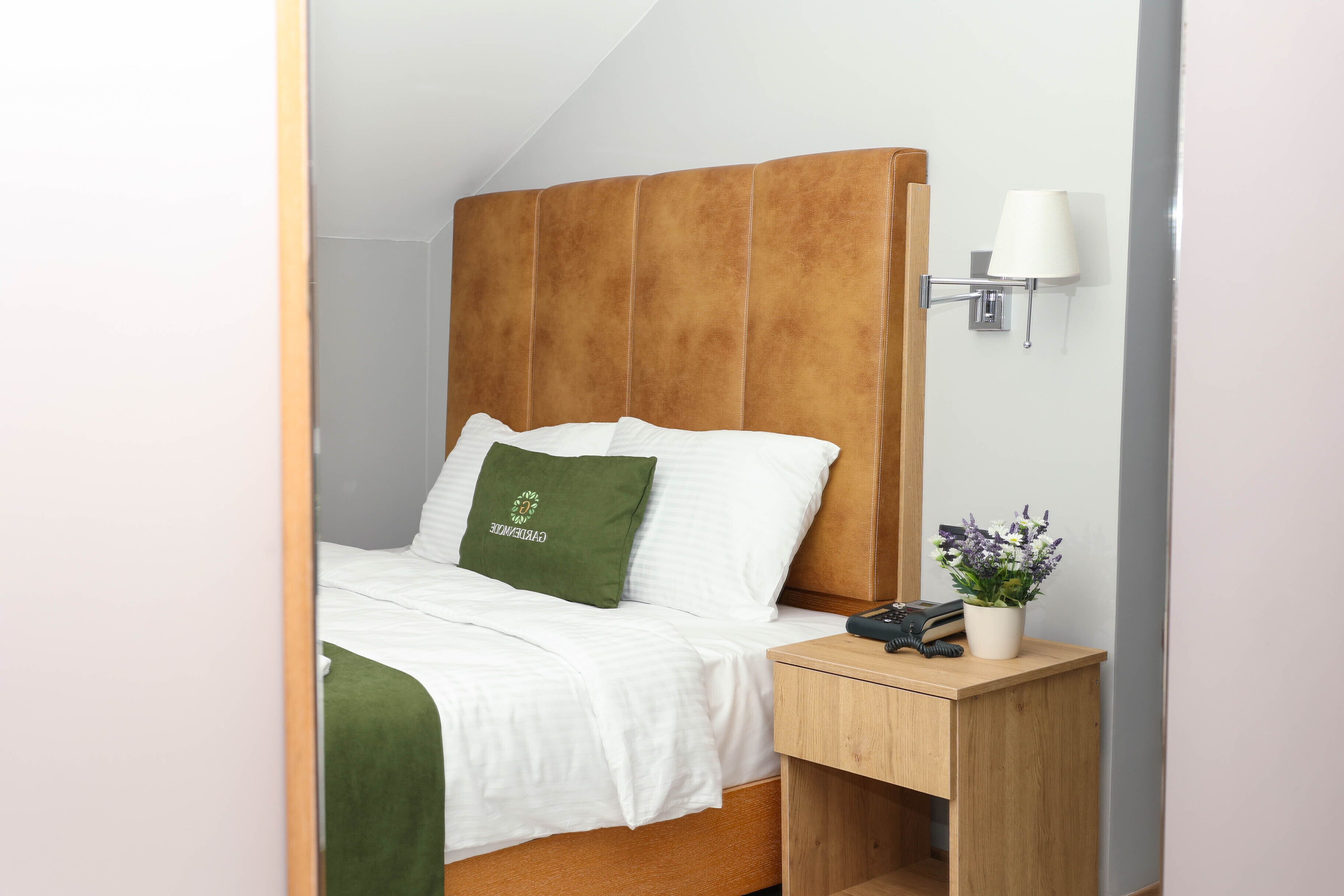 A neatly made bed with a green pillow, a wooden bedside table with a lamp, and a phone.